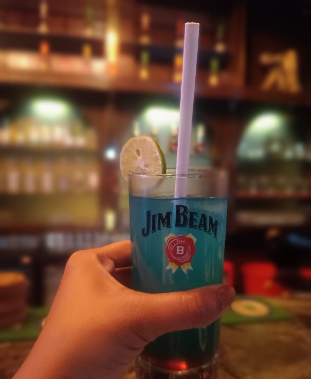 A vivid blue signature cocktail garnished with lime against the back bar
